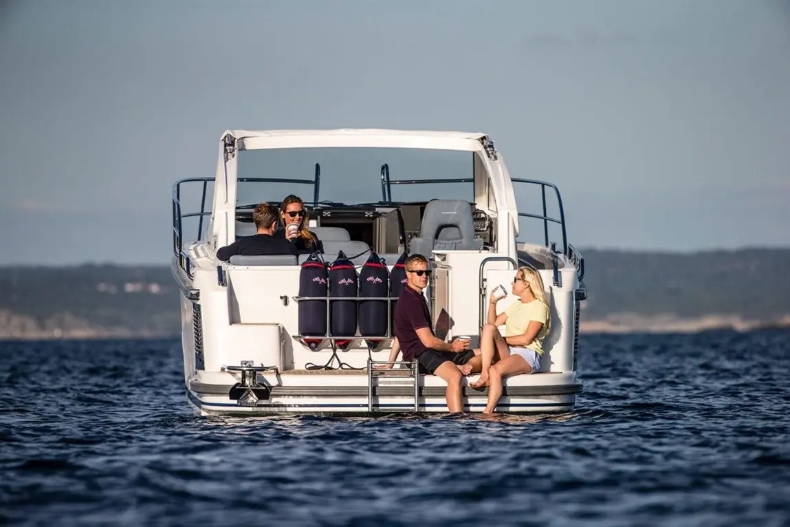 Friends enjoying drinks on a sleek boat, with the sun shining, surrounded by calm waters and distant hills.
